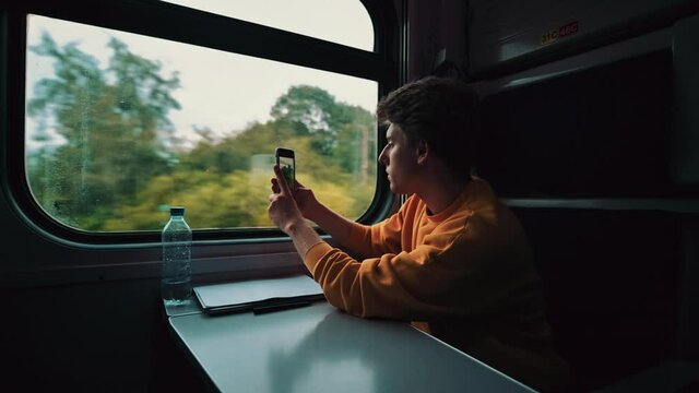 Young man travels by train and talks on the phone with a serious person. Guy is talking on the phone in the railway train by the window.