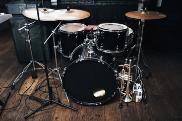 A black drum kit with cymbals and a microphone stand are on stage and next to them are two trumpets (alto and bass) and a white tambourine. The concept of a live concert of a jazz band.