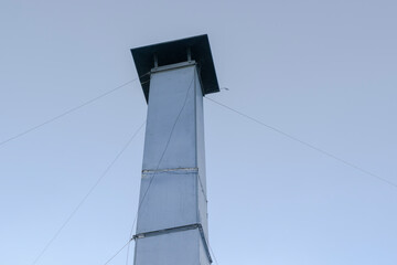 Old metal pipe against the sky. Chimney made of stainless, shiny metal. Lashing cables.