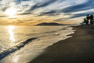 Sunset over the beach of Torre de Benagalbon, a coastal town of Andalucia in Spain, with 2 paddle boarder on the sea