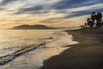 Sunset over the beach of Torre de Benagalbon, a coastal town of Andalucia in Spain, with 2 paddle boarder on the sea
