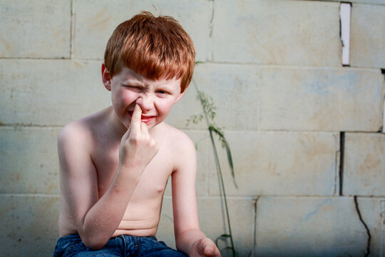 Young redheaded boy picking nose with shirt off