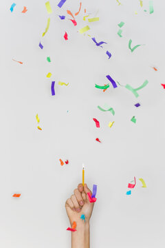Hand holding a lit birthday candle with confetti falling