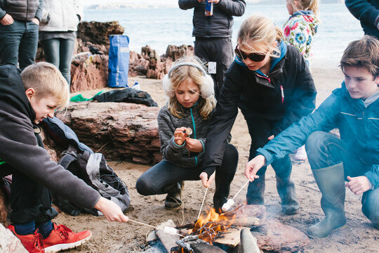 A group of friends toasting marshmallows over a fire on a beach.