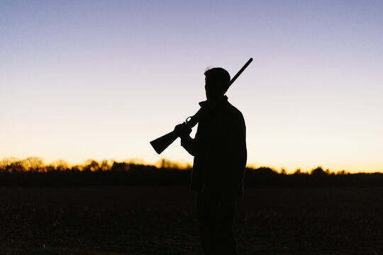 Silhouette of hunter holding gun on shoulder during hunt