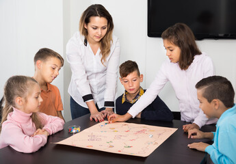 Smiling kids sitting at table with board game and dice at school