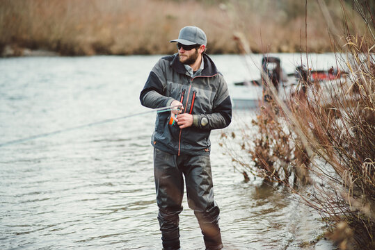 Fly fisherman standing in river fighting a large fish he is hooked up to.