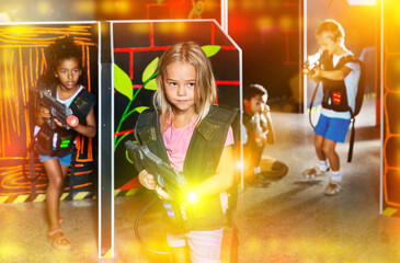 Cute preteen girl with laser pistol playing laser tag with friends on dark labyrinth