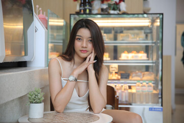 Portrait of Asian Young happy woman sitting alone in modern coffee shop interior.
