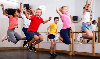 Cheerful preteen boys and girls having fun in group dance class, jumping with female coach ..