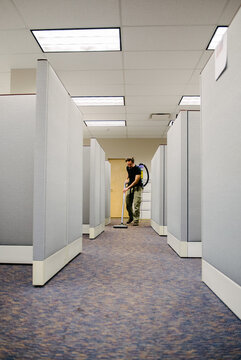 After hours janitor vacuums carpets in an office building