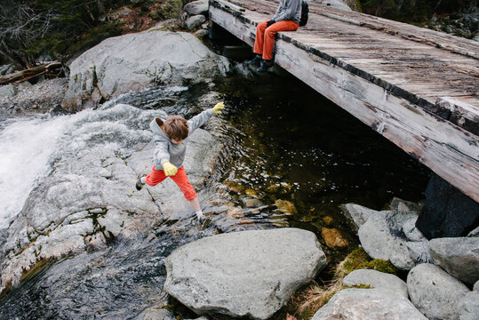 Boy hops from rock to rock across a mountain stream