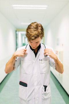 A doctor standing in the hall of a hospital with and putting his stethescope around his neck