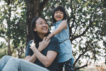 Asian little daughter hug her mom with smile in the park. Concept for family relationship and relaxing time.