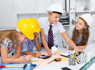 Teens in color helmet engineers discussing draft at the table.