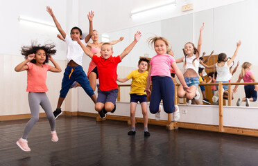 Obraz premium Group of happy sporty kids with female teacher training in modern dance studio, jumping together..