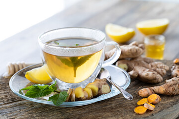 Clear glass tea cup of green tea with ginger and turmeric against a sunny window.