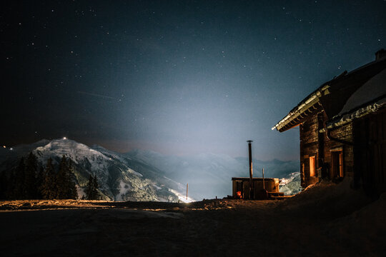 wooden alpine cabin with jacuzzi in snowcovered mountain landscape at night under starry sky