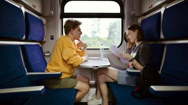 Cute couple man and woman ride the train, sit in the train compartment at the table and communicate. Colleagues go on a business trip and read the text on the documents.