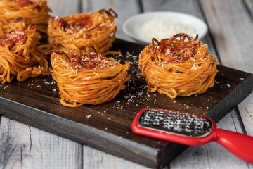Spaghetti nest appetizers on a wooden board sprinkled with parmesan cheese.