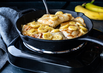 Banana Foster cooking in a cast iron skillet against a dark background.