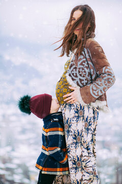 Beautiful pregnant woman with her little son outside while snowing