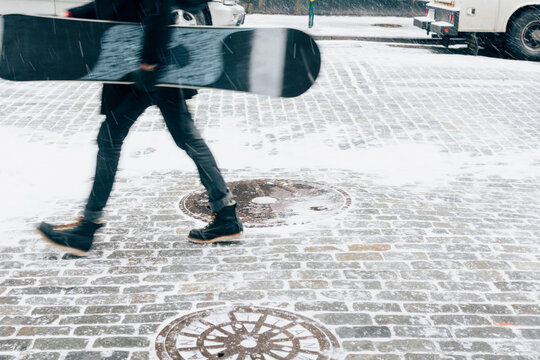 Man carrying snowboard, walking across street during snowstorm. New York City.