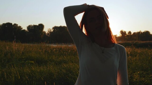 [4k] backlight silhouette of beautiful ginger woman in late evening sun in nature playing with her hand in her long hair