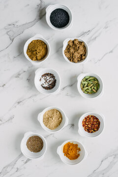 overhead of various spices and seeds in white bowls on a clean marble background