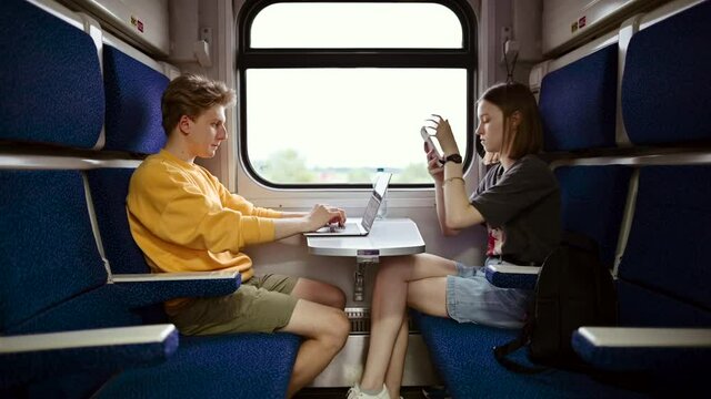 Beautiful young couple in roe deer clothes ride in a compartment train and use gadgets, a man works on a laptop and a woman uses the Internet on a smartphone.