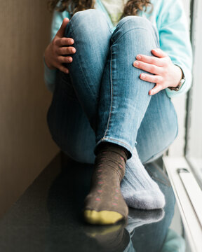 anonymous woman with mismatched socks sitting in a window
