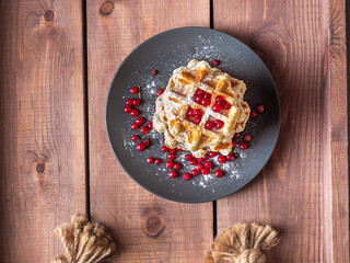 Homemade waffles with cottage cheese sprinkled with powdered sugar on a black plate and red currant berries