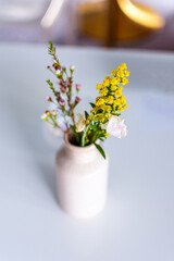 Colorful flowers in a white vase on a table with blurred background with room for copy text
