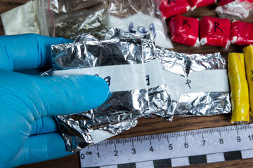 evidence of smuggling traffic: Packaging of a narcotic substance in the hand of a forensic expert against the background of other arrested materials, cocaine, heroin, spice