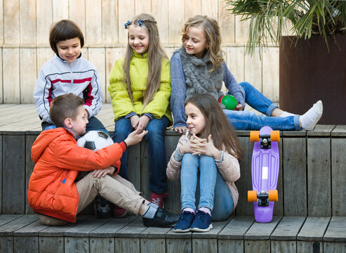 Group of children in casual clothing with ball and skateboard chatting outdoors
