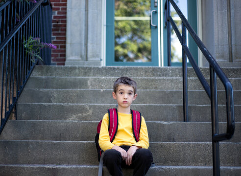 Boy sits on steps in front of school looking unimpressed