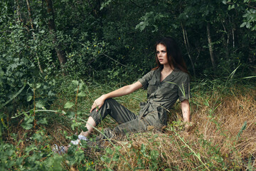 woman in jumpsuit sneakers sits on the grass in the forest