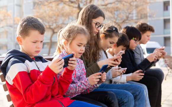 Group of children playing with smartphones outdoors at sunny spring day