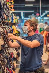 Fototapeta na wymiar Serious man blue in blue t-shirt choosing shoes in store, wearing blue face mask protect from virus COVID, public personal health control measure, shopping during pandemic, buying new clothing