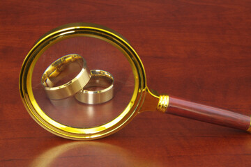 Golden wedding rings and magnifying glass on wooden table.
