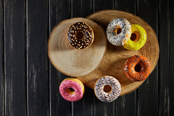 Multicolored donuts with glaze and sprinkles on wooden coasters on a black background