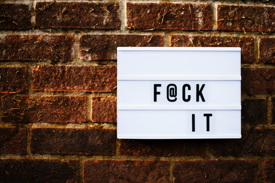 The words F@ck It spelled out on a cinematic lightbox on a brick wall.