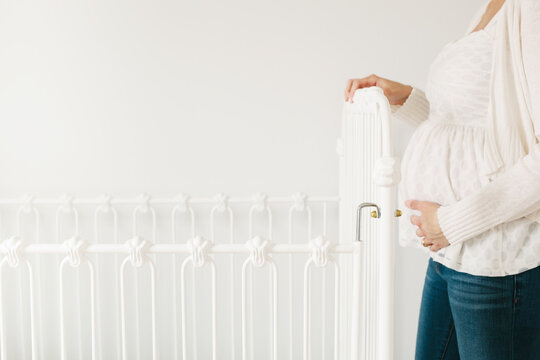 pregnant woman standing next to a crib in a nursery