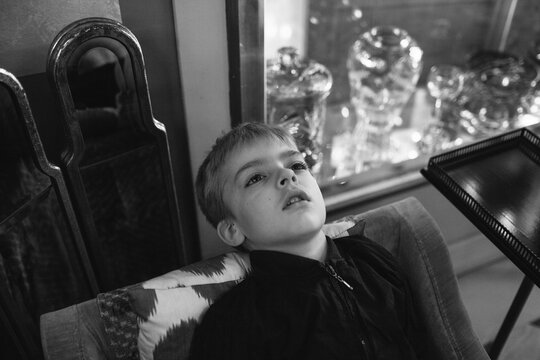 Boy leans back on chair in a room with old fashioned objects.