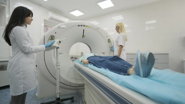 Female patient is undergoing CT or MRI scan under supervision of two qualified radiologists in modern medical clinic. Patient lying on a CT or MRI scan table, leaves the machine