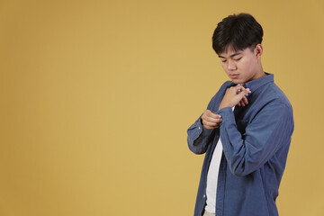portrait of handsome young asian man in casual clothing buttoning sleeves shirt cuff. yellow background