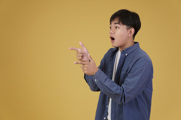 portrait of handsome young asian man dressed casually  pointing fingers at copyspace. yellow background