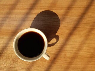 Top view of coffee cup on wooden table with natural light and shadow in the morning.
