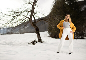 portrait of blonde girl in a yellow winter coat  on the snow in the mountains in winter near a forest
