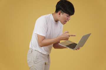 aggressive angry upset furious young asian man scolding screaming yelling on laptop computer isolated on yellow background
